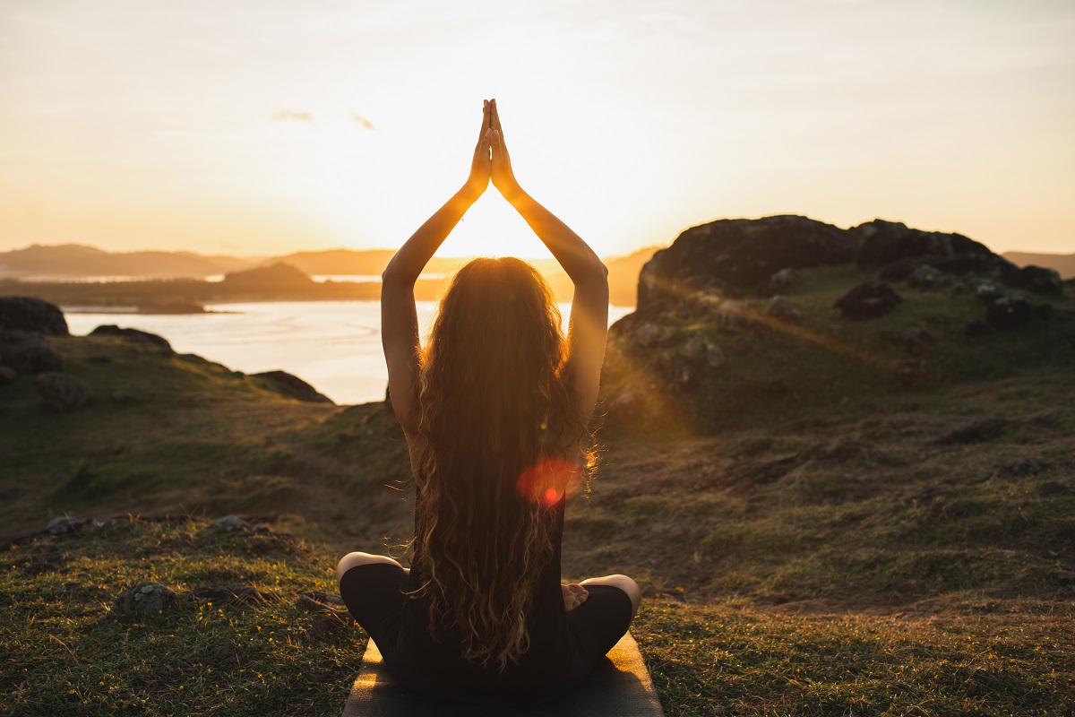 young woman meditating with prayer hands on beach during sunset spiritual prayers