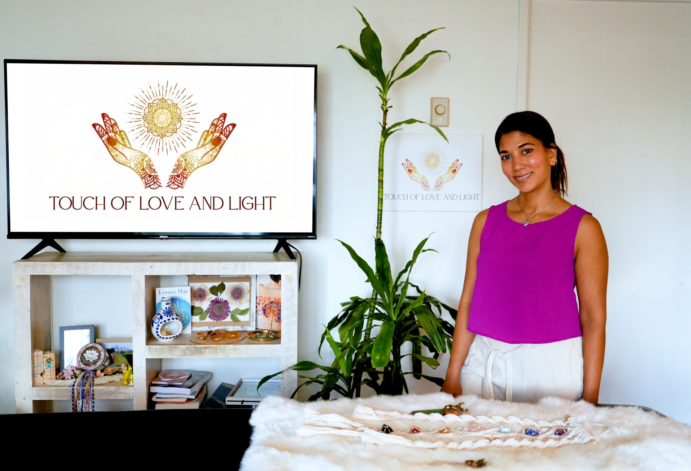 women standing behind massage table with crystals on top of it and logo on TV screen