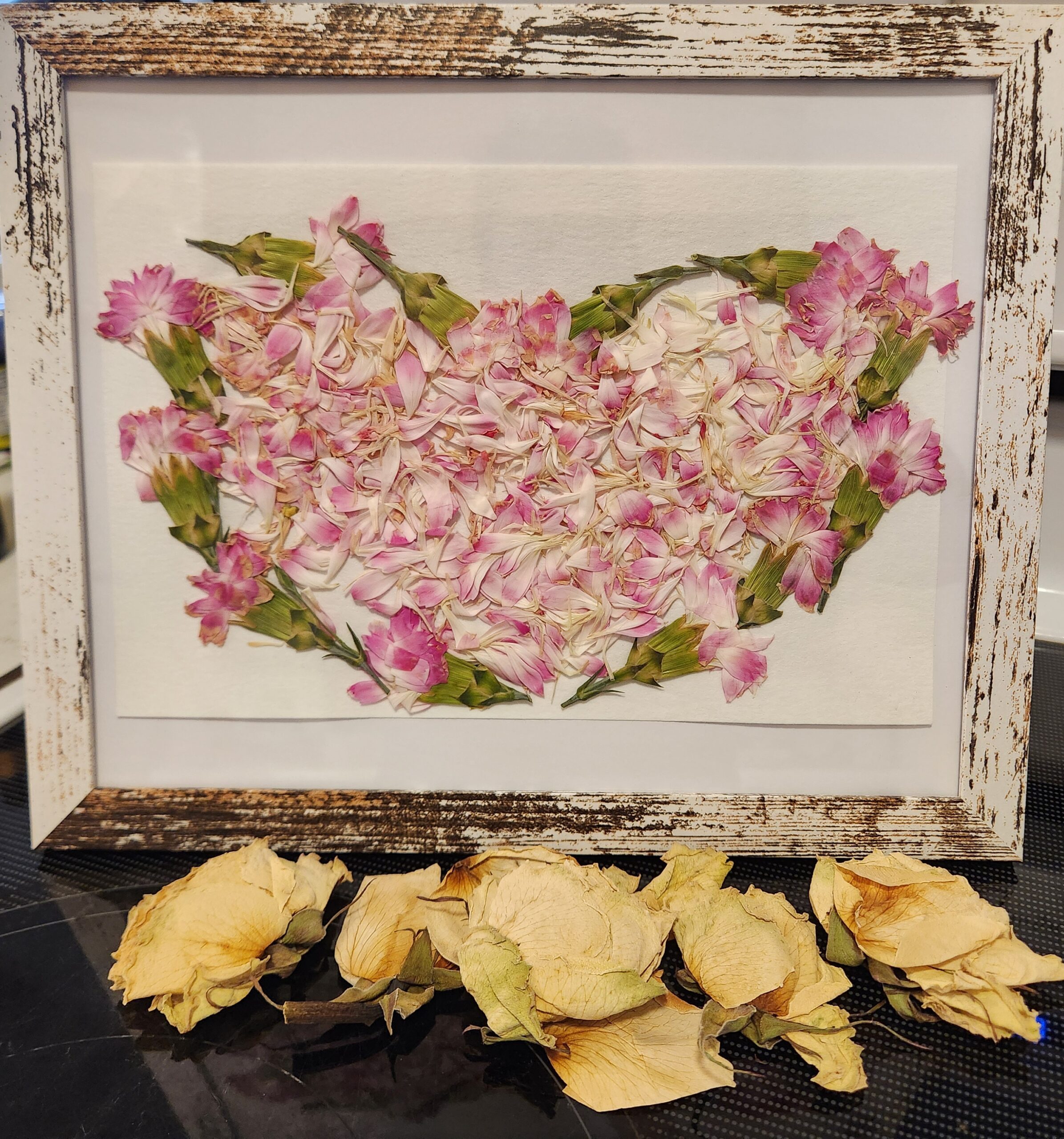 heart-shaped pressed flowers in a white wooden frame with roses